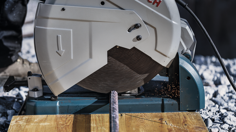 Metal cutting saw slicing through a steel rod with sparks flying.