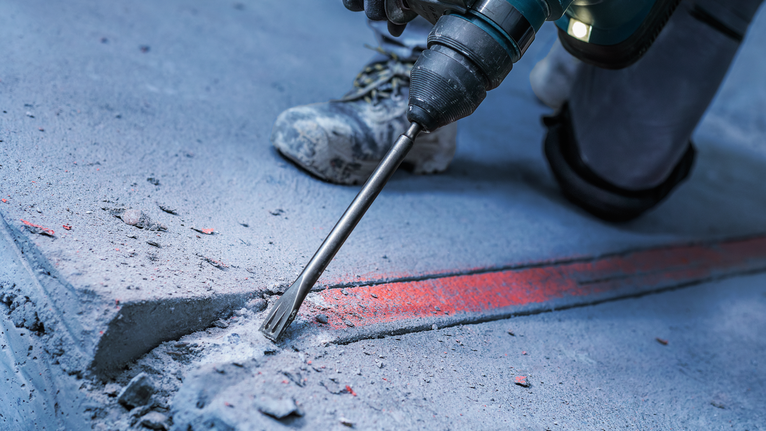 Person wearing safety equipment uses a rotary hammer to break concrete floor.
