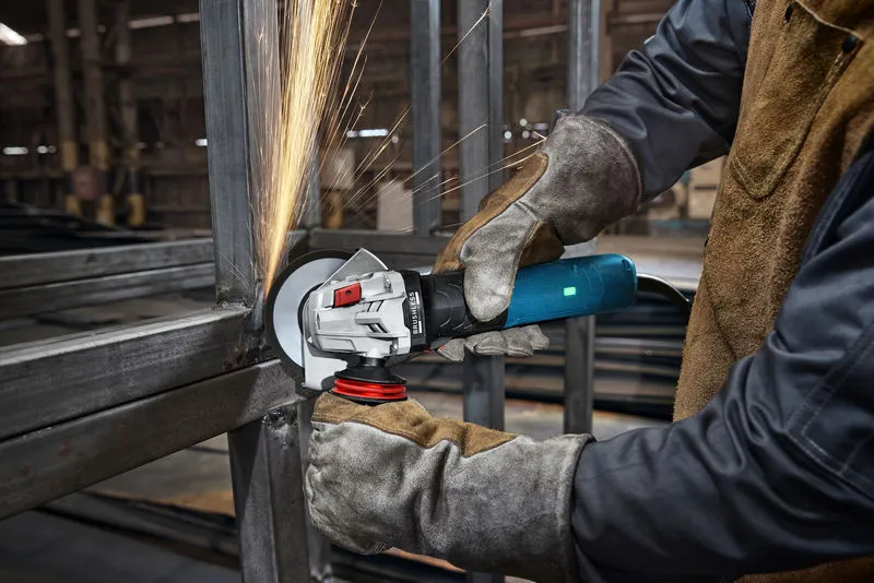 A person wearing safety equipment grinds metal, creating sparks in an industrial setting.