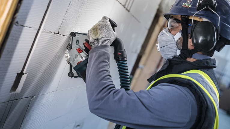 Person wearing safety equipment uses a wall chaser to cut grooves in concrete blocks.