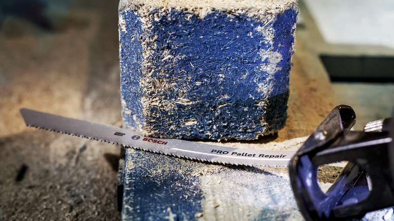 Saw blade and power tool cutting through a blue painted block of wood.
