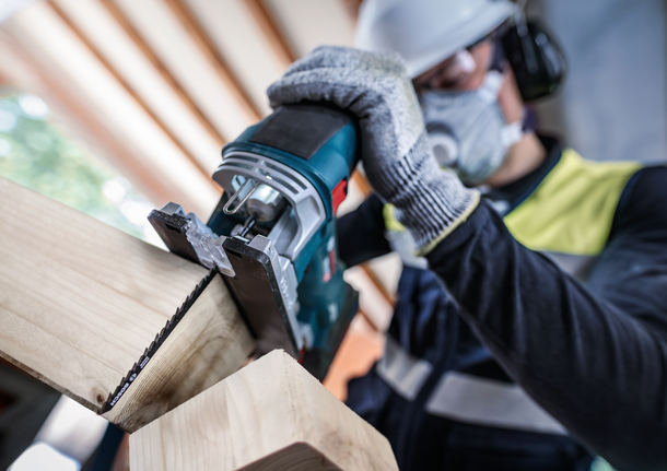 Person wearing safety equipment cuts wood with a jigsaw.