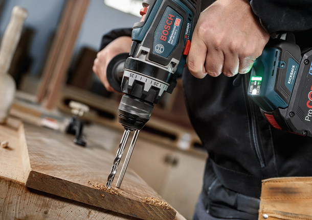Person using a cordless drill to make a hole in a wooden board.