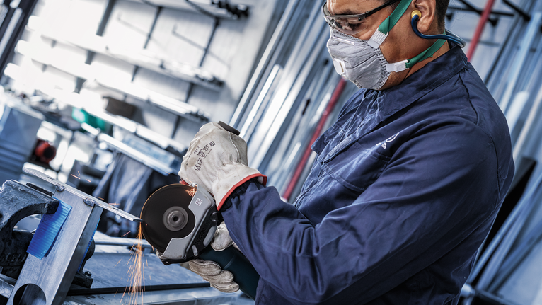 A person wearing safety equipment grinds metal, producing sparks.