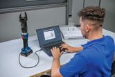 A person connects a cordless hydraulic cutting tool to a laptop for data analysis.