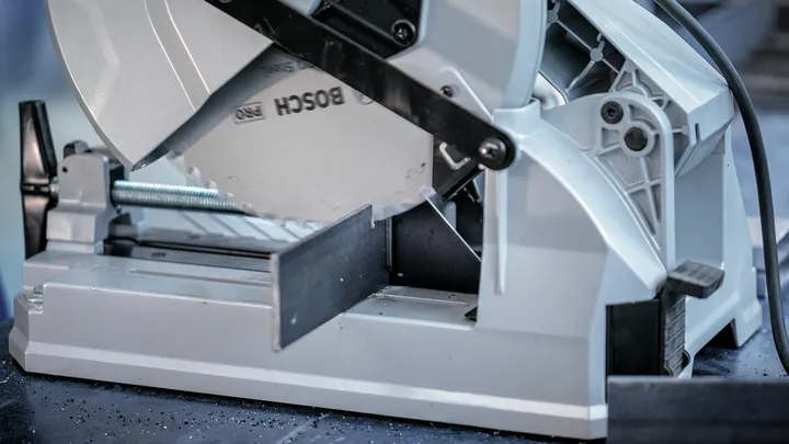 Metal cutting saw blade slices through a steel bar in a workshop setting.