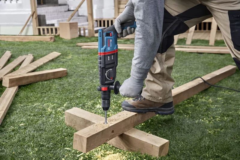 A person wearing safety equipment drills into a wooden beam at a construction site.