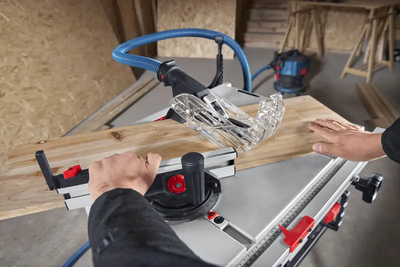 A person pushes wood through a table saw in a workshop.