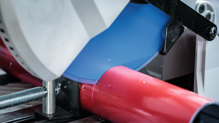 Metal-cutting saw slices through a red pipe secured in a clamp.
