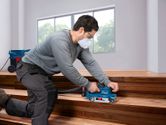 A person wearing safety equipment sands wooden stairs with a belt sander.