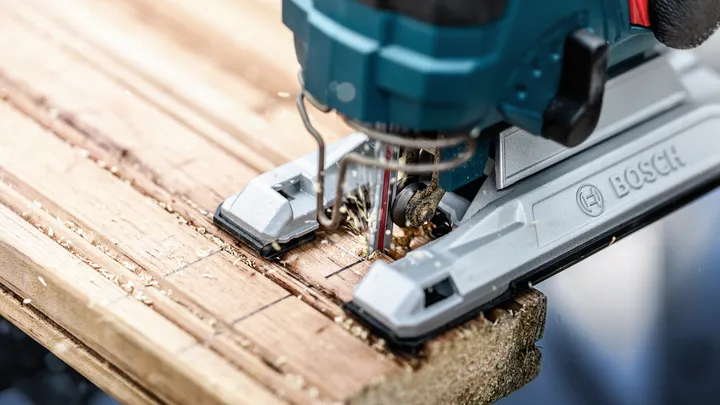 Jigsaw cutting through marked wooden plank.