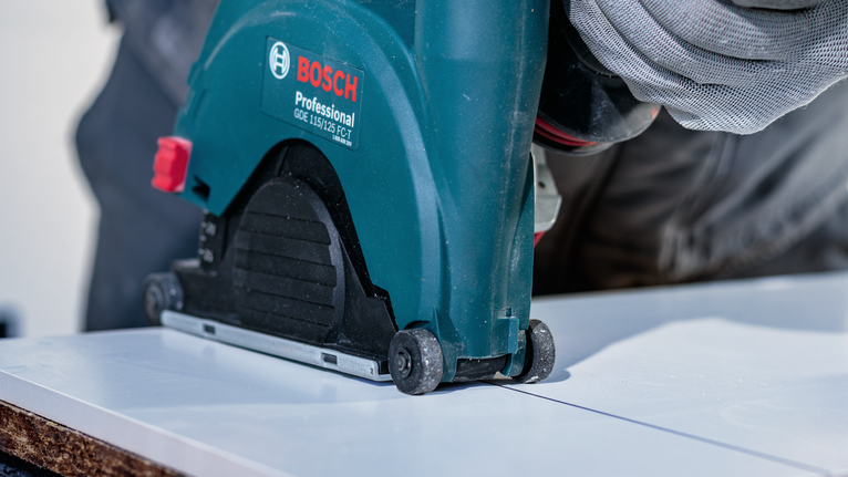 Person wearing safety equipment guiding a power saw to cut a straight line on a board.