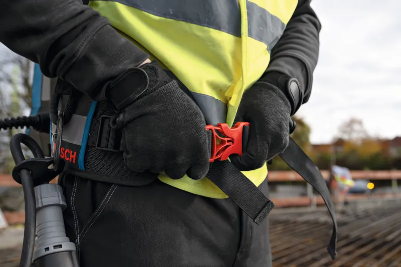 A person wearing safety equipment secures a belt while holding a concrete vibrator.
