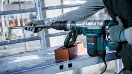 Person wearing safety equipment uses a rotary hammer to chisel a brick.
