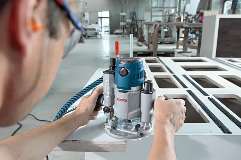 A person wearing safety equipment uses a router to shape the edge of a wooden board.