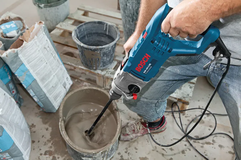 A person mixes construction material in a bucket using an impact drill.