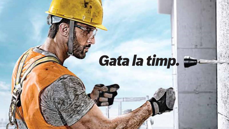 Un muncitor cu cască galbenă folosește un burghiu pe un perete de beton.