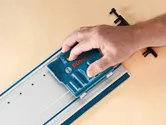 O persoană folosește un accesoriu albastru de sistem pe o șină metalică așezată pe o suprafață de lemn.