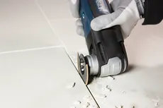 O persoană purtând echipament de siguranță taie plăci ceramice cu o unealtă multifuncțională oscilantă.