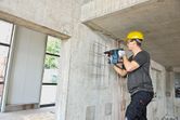 O persoană purtând echipament de siguranță găurește un perete de beton folosind un ciocan rotopercutor.