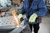 O persoană care poartă echipament de siguranță folosește o polizor unghiular pentru a tăia metalul, creând scântei.