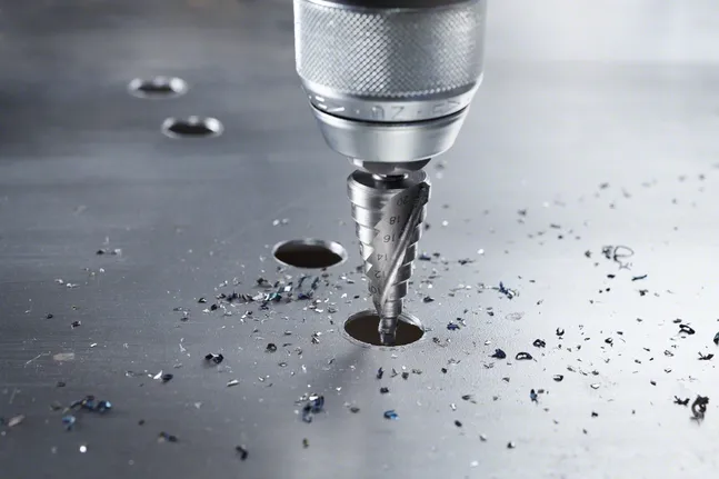 Burghiu în trepte care creează o gaură într-o tablă metalică cu așchii împrăștiate.