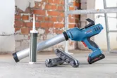 Pistol de silicon fără fir pe o podea de beton lângă cartușe de silicon într-o zonă de construcții.