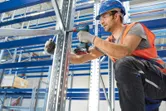 O persoană care poartă echipament de siguranță fixează un cadru metalic folosind o bormașină electrică fără fir.