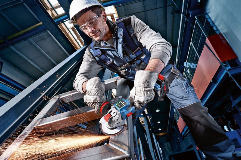 O persoană care poartă echipament de siguranță șlefuiește o grindă metalică cu o unealtă electrică, producând scântei.