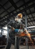 O persoană care poartă echipament de siguranță taie metalul cu o polizor unghiular, creând scântei.