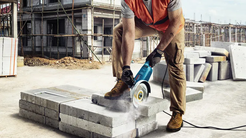 O persoană purtând echipament de siguranță folosește o mașină de tăiat blocuri de beton pe un șantier.