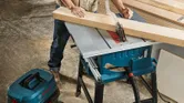 O persoană purtând echipament de siguranță taie lemn cu un ferăstrău circular într-un atelier.