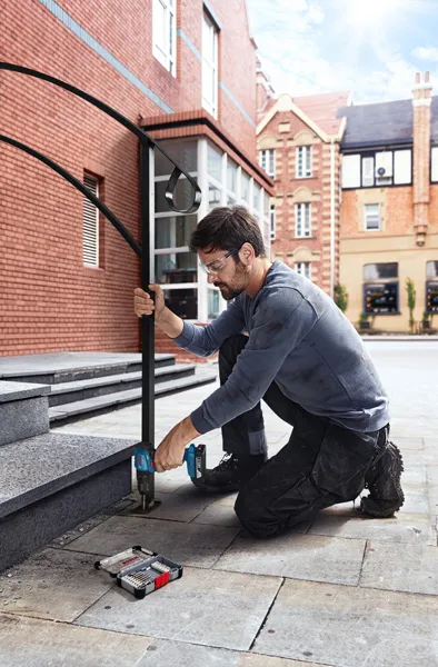 O persoană purtând echipament de siguranță găurește trepte de piatră, instalând o balustradă metalică.