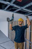 Persoană purtând echipament de siguranță instalează gips-carton folosind o șurubelniță fără fir.