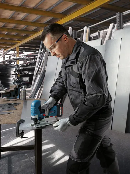 O persoană care poartă echipament de siguranță taie o tablă de metal cu un ferăstrău vertical fără fir.