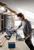 O persoană care poartă echipament de siguranță taie o scândură de lemn cu un ferăstrău circular într-un atelier.