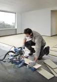 O persoană care poartă echipament de siguranță folosește un ferăstrău cu mitră pentru a tăia parchetul laminat.