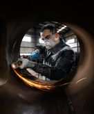 O persoană care poartă echipament de siguranță macină metalul în interiorul unei țevi mari, creând scântei.