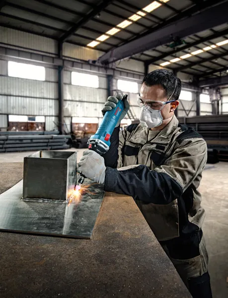O persoană care poartă echipament de siguranță folosește o polizor drept pe o tablă metalică.