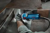 O persoană care poartă echipament de siguranță șlefuiește o cusătură metalică sudată cu o polizor drept.