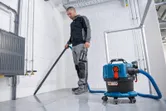 O persoană care poartă echipament de siguranță folosește un aspirator umed și uscat pentru a curăța o podea cu gresie.