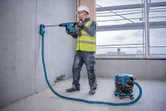 O persoană purtând echipament de siguranță găurește un perete de beton folosind un sistem de extracție a prafului.