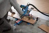 O persoană care poartă echipament de siguranță taie parchetul laminat cu un ferăstrău circular cu mitră.