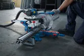 O persoană care poartă echipament de siguranță taie profile metalice cu un ferăstrău circular cu mitră.