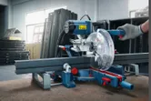 O persoană care poartă echipament de siguranță operează un ferăstrău cu mitră pentru a tăia o bară metalică.