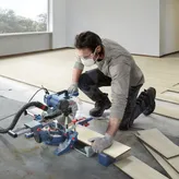 O persoană care poartă echipament de siguranță taie parchetul laminat cu un ferăstrău cu mitră.