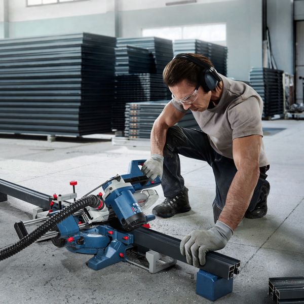 O persoană care poartă echipament de siguranță folosește un ferăstrău pentru tăierea metalelor pentru a tăia un profil de oțel.