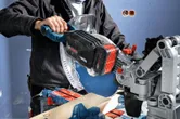 O persoană care poartă echipament de siguranță folosește un ferăstrău cu mitră și un pachet de baterii de 8,0 Ah pentru a tăia lemn.