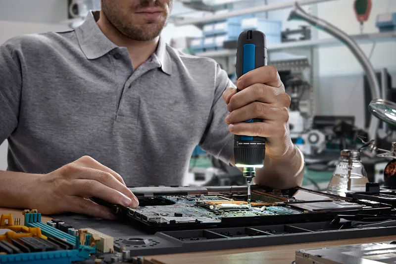 Persoană care folosește o șurubelniță fără fir pentru a asambla componente electronice pe o placă de circuit.