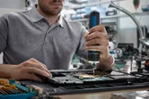 Persoană care folosește o șurubelniță fără fir pentru a asambla componente electronice pe o placă de circuit.